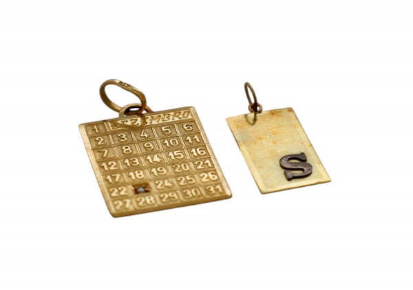 Par de pingentes em ouro 18 quilates (750/1000), sendo o primeiro uma placa retangular lisa com a letra S aplicada em relevo, provavelmente em acabamento oxidado ou esmaltado; o segundo, uma placa em