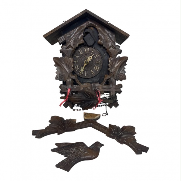 Relógio cuco de parede, com caixa em madeira entalhada em decoração de folhas, mostrador circular com algarismos romanos e ponteiros metálicos. Mede 33 cm de altura. Acompanha ave e um dos contrapesos