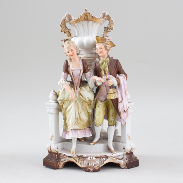 Escultura em biscuit representando casal em trajes de época junto a jardineira ornamental, rica em detalhes e aplicações douradas, medindo 26 cm de altura, apresentando desgastes compatíveis com o tem