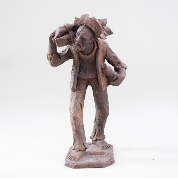 Escultura em barro representando trabalhador carregando feixe de lenha aos ombros, sobre base integrada, com plaqueta identificando o artista Zé do Carmo Goiana; altura: 33 cm; apresenta marcas do tem