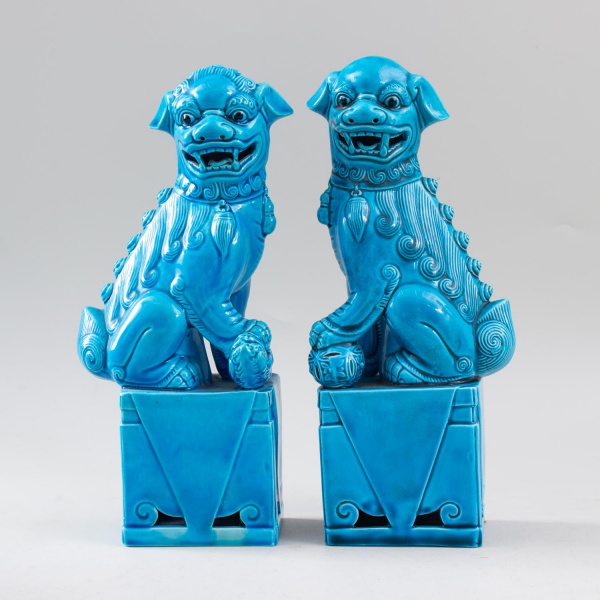 Par de esculturas orientais em porcelana esmaltada azul-turquesa, representando cães de fó (Fu Dogs) sobre pedestais, ricamente decorados em relevo, medindo 26 cm de altura cada, com marcas do tempo.
