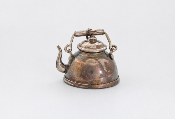 Miniatura de chaleira em prata de lei, teor 900, com alça móvel e tampa articulada. Peso 11 g e Altura: 1 cm. Apresenta marcas de uso, oxidação e desgastes compatíveis com o tempo.