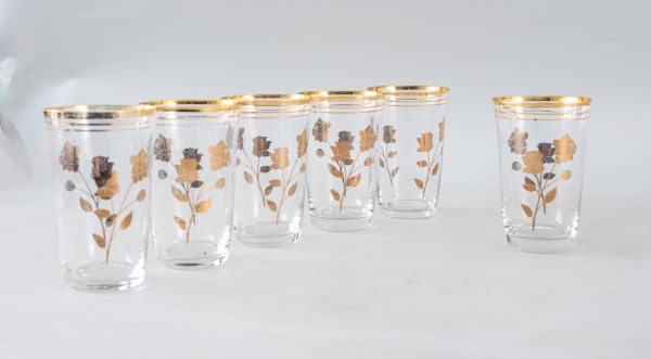 Conjunto com 6 copos em vidro transparente, decorados com delicados motivos florais e frisos dourados na borda, de estilo clássico, medindo 11 cm de altura, com bicados e desgastes no dourado.