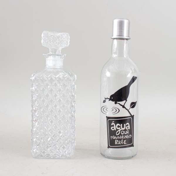 Lote com duas garrafas para bebidas, sendo uma em cristal lapidado com tampa e uma em vidro. Maior medindo 28 cm de altura. Apresentam marcas do tempo e de uso.