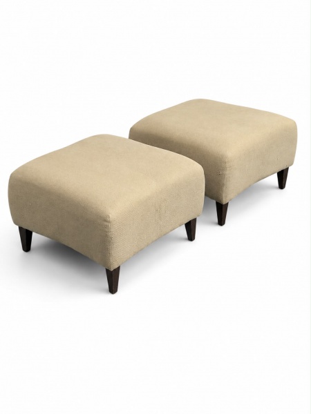 Par de pufes estofados em tecido na cor bege, com linhas retas e pés em madeira, de design contemporâneo, medindo 40 cm de altura e 60 x 60 cm cada. Apresentam sinais de uso e marcas do tempo, um dos
