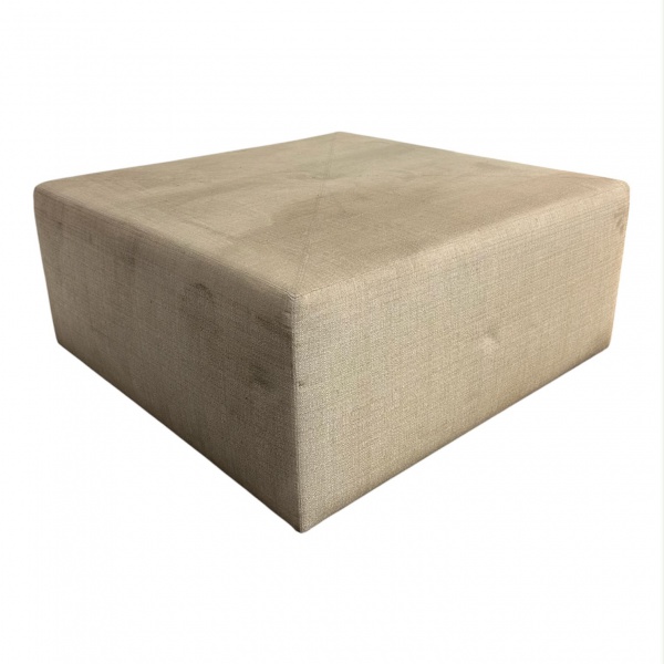 Pufe estofado em tecido na cor bege, de design contemporâneo e formato quadrado, medindo 38 cm de altura e 84 x 84 cm, apresentando marcas de uso e sinais do tempo.