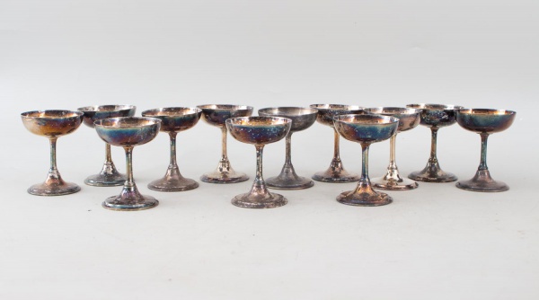 Lote composto por 12 taças baixas em metal prateado, de corpo liso sobre haste curta e base circular. Altura: 9 cm. Apresentam sinais de uso, oxidação, desgastes e manchas no banho, sendo vendidas no