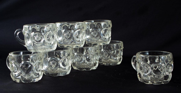 Conjunto com oito pequenas canecas em vidro incolor lapidado, decoradas com motivos circulares e alças integradas. Altura: 6 cm. Vendidas no estado, com marcas de uso compatíveis com o tempo.