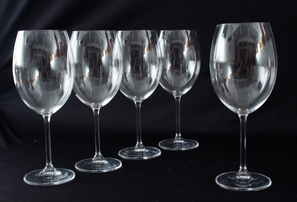 Conjunto com cinco taças em cristal incolor, de bojo liso e haste alta. Altura: 24 cm. Apresentam marcas de uso compatíveis com o tempo.