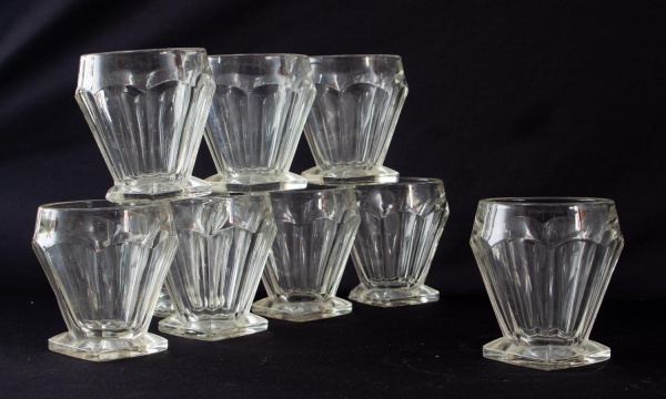 Lote com nove copos em vidro incolor prensado, de mesmo modelo, com base quadrada. Altura: 10 cm. Apresentam marcas de uso e desgastes compatíveis com o tempo.