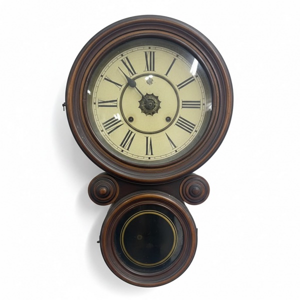 Relógio de parede Waterbury, em caixa de madeira torneada, mostrador esmaltado com algarismos romanos e compartimento superior para gongo. Comprimento: 55 cm. Não testado. Apresenta marcas de uso, des