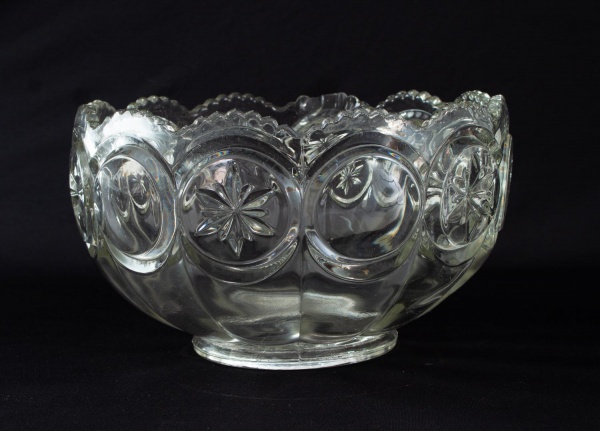 Centro de mesa em vidro incolor moldado, de formato circular com decoração em medalhões em relevo e borda ondulada. Altura: 16 cm. Apresenta marcas de uso e desgastes compatíveis com o tempo.