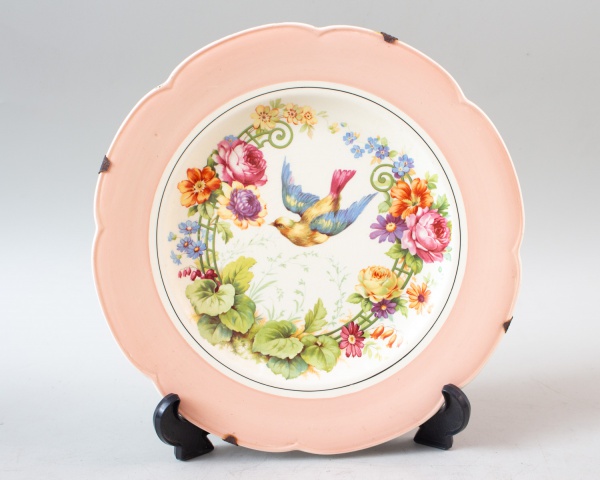 Prato decorativo em porcelana inglesa Woods Ivory Ware, com borda ondulada em tom rosado e centro com pintura policromada de ave em meio a flores, medindo aproximadamente 27 cm de diâmetro; apresenta