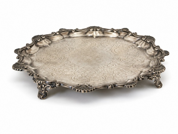 Bandeja circular em prata de lei teor 925, com aba recortada e borda em relevo de inspiração rococó, decorada com elegante trabalho de cinzelado em arabescos no espelho, medindo 27 cm de diâmetro e pe