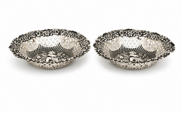 Par de cestas decorativas em prata de lei teor 925, com bordas vazadas em rica ornamentação de inspiração rococó e bojos decorados em relevo com figuras de querubins, medindo 12 cm de diâmetro cada e