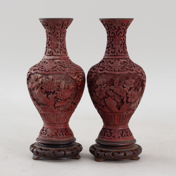 Par de vasos orientais em resina cinábrio, ricamente decorados em alto-relevo com motivos florais e arabescos vazados, interior esmaltado em azul, acompanhando bases em madeira entalhada, medindo 19 c
