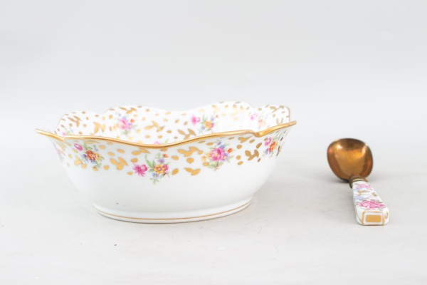 Saladeira em porcelana francesa Limoges, ricamente decorada com motivos florais policromados e detalhes em douração, acompanhada de colher de servir com cabo em porcelana decorado em padrão correspond