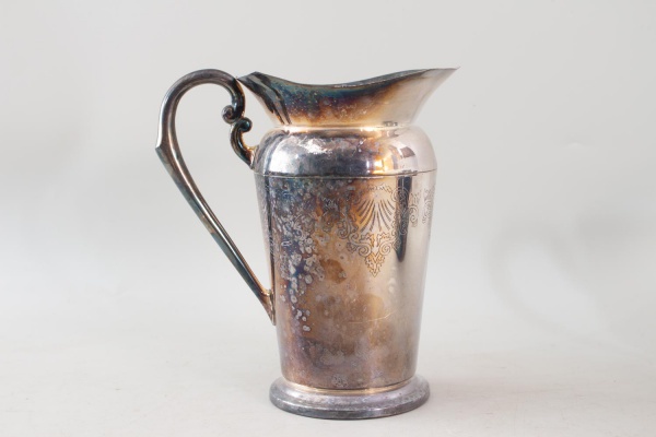 Jarra em metal espessurado a prata da marca Eberle Prat Forte, de corpo cilíndrico com decoração gravada, alça vazada e bocal recortado, medindo 22 cm de altura, apresentando marcas de uso, oxidação e