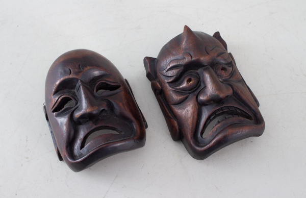 Par de máscaras japonesas em madeira entalhada, da Era Meiji, representando personagens do teatro Noh, uma com feição humana e outra demoníaca (Hannya), em acabamento marrom-escuro, medindo 12 cm de a