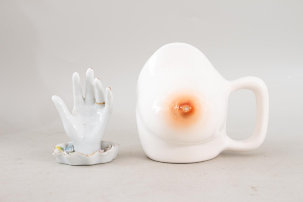 Conjunto com duas peças exóticas em cerâmica esmaltada, composto por caneca em formato de seio medindo 15 cm e cinzeiro em formato de mão aberta medindo 12 cm, apresentando pintura policromada, detalh