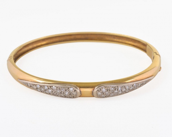 Pulseira rígida em ouro 18K, peso 16,6 g, com diâmetro maior de 6,1 cm e menor de 4,7 cm. Modelo ovalado com fecho de segurança e detalhe frontal em ouro branco cravejado com pequenas pedras brilhante