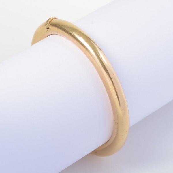 Pulseira rígida em ouro 18K, peso 26 g, com diâmetro maior de 6,2 cm e menor de 5,4 cm. Modelo tubular liso com acabamento polido e fecho de encaixe com trava de segurança. Peça robusta, de estilo clá
