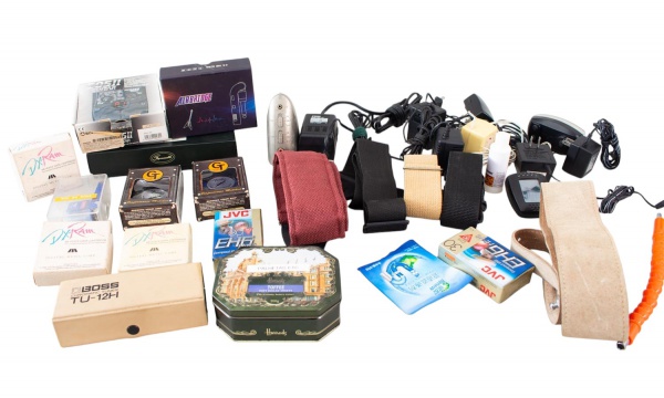 Lote composto por acessórios diversos para instrumentos musicais e equipamentos eletrônicos, incluindo correias para guitarra, afinador eletrônico Boss TU-15, pedal Zoom 505 II, adaptadores, fontes de