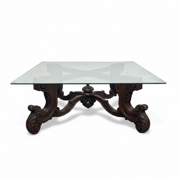 Mesa de centro em madeira nobre entalhada, com base de inspiração clássica composta por pés recurvos e travamento central ornamentado, tampo quadrado em vidro incolor medindo 100 x 100 cm, altura de 4