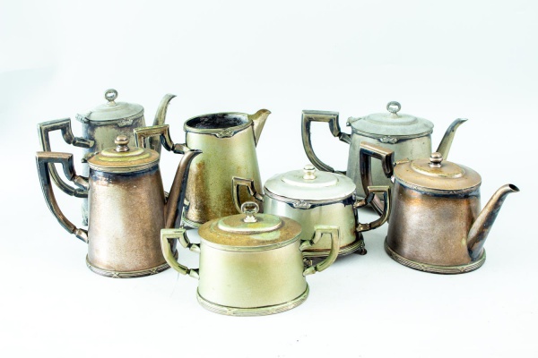 Conjunto para chá e café em metal espessurado, composto por 7 peças, sendo 3 bules, 2 açucareiros e 2 leiteiras, com alças angulares e decoração em frisos, medindo o maior 18 cm de altura, apresentand