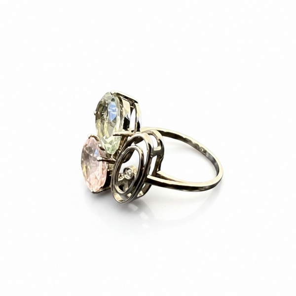 Anel de autoria da Joalheria Lisht em ouro branco 18k, peso aproximado de 5 g, aro 16. Apresenta dois topázios em lapidação oval um verde (prasiolita/topázio verde) em corte pera e um rosa (topázio ro