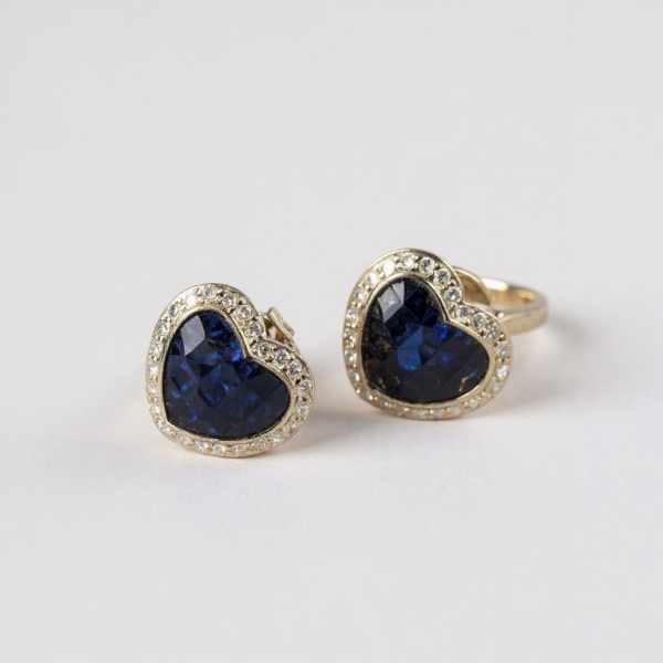 Brinco coração em ouro amarelo, peso 3,6g, com safira azul de corte coração em pavê francês, contornada por halo de diamantes redondos. Fecho clique.