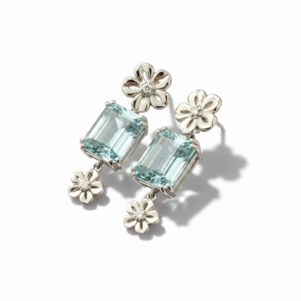 Brinco pendente em ouro branco, peso 7,8g, composto por topping flor com diamante central, topázio azul de corte esmeralda em garras e flor pequena com diamante na base. Design romântico e elegante, f