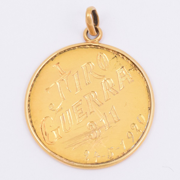 Pingente em ouro 18k com a inscrição Tiro guerra 311 24-5-1920. Peso 5g. Mede 2,5cm.