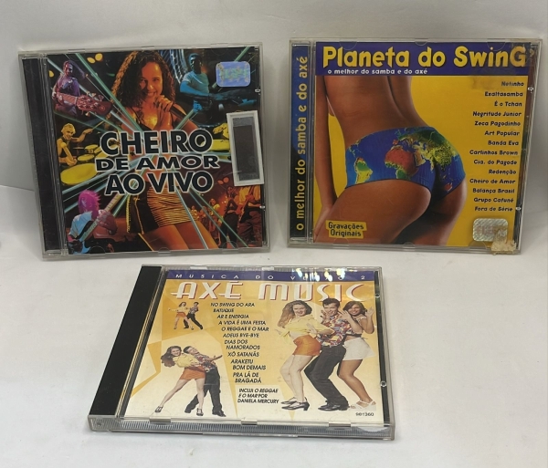 Lote com três CDs originais de axé e pagode contendo os álbuns Cheiro de Amor ao Vivo, a coletânea Planeta do Swing e o CD promocional Axé Music volume 2. Discos de música brasileira de grande sucesso