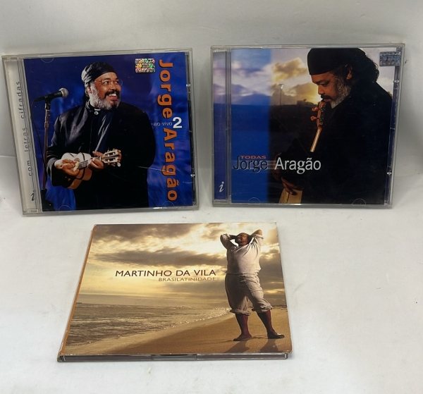 Lote com três CDs de samba e MPB reunindo os álbuns Jorge Aragão ao Vivo 2 e Todas, do sambista Jorge Aragão, além do álbum Brasilatinidade, do cantor e compositor Martinho da Vila. As obras contam co