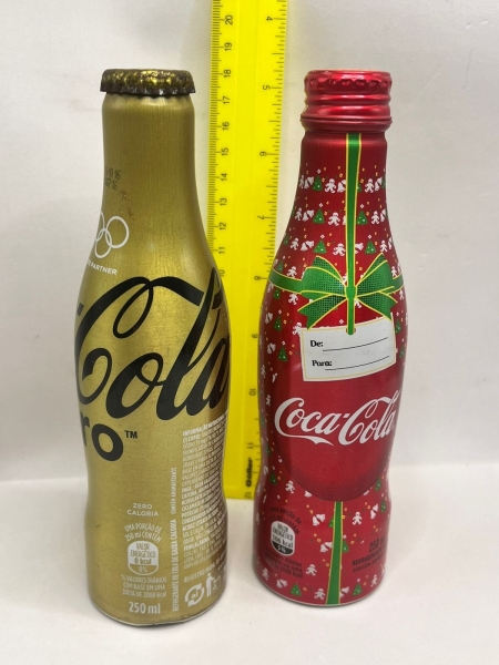 Garrafa de Alumínio Cheias com Líquido Coca-Cola Zero Edição Limitada Olímpiadas e Garrafa de Alumínio Coca-Cola Temática de Natal, ambas com capacidade de 250ml. As peças colecionáveis apresentam aca
