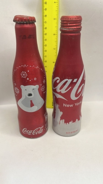 Conjunto de duas garrafas de alumínio colecionáveis da Coca-Cola, sendo uma edição especial com o Urso Polar e outra temática da cidade de Nova York. As peças em metal apresentam acabamento em tom ver