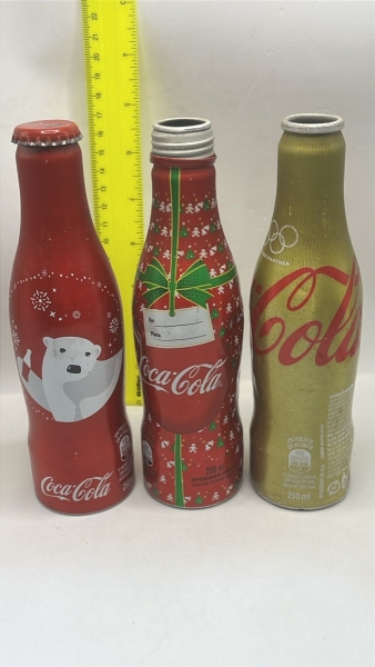 Conjunto de três garrafas colecionáveis de alumínio Coca-Cola, sendo duas edições natalinas com estampa de urso polar e laço de presente, além de uma versão dourada comemorativa das Olimpíadas. As peç