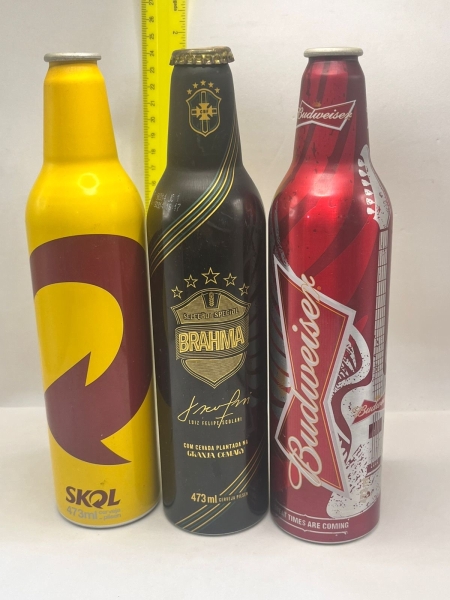 Conjunto de três garrafas de cerveja colecionáveis em alumínio de 473ml, contendo uma Skol, uma Brahma Seleção Especial com assinatura de Luiz Felipe Scolari e uma Budweiser temática. As peças exibem