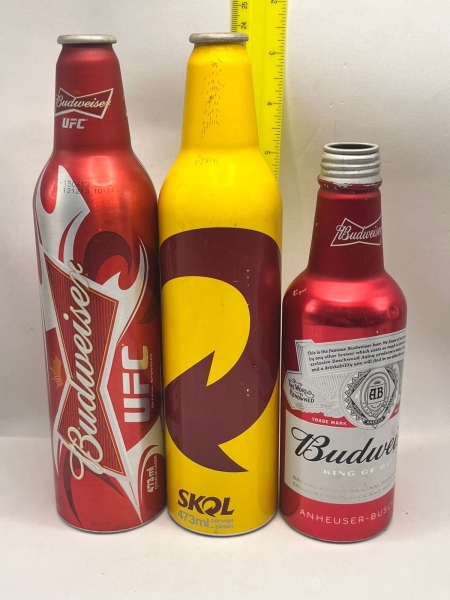 Conjunto de três garrafas de cerveja colecionáveis em alumínio, sendo uma Budweiser edição especial UFC de 473ml, uma Skol de 473ml e uma garrafa Budweiser King of Beers de menor porte. As peças possu