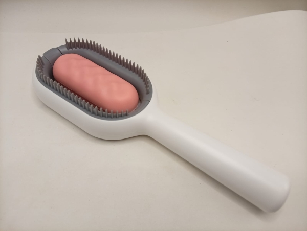 Escova Removedora de Pelos de Cães e Gatos em Plástico Branco com Cabo Anatômico. O Modelo Possui Base Ovalada com Cerdas em Silicone Cinza e Rolo Central Emborrachado na Cor Rosa para Limpeza de Esto