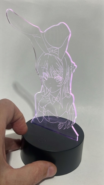 Luminária LED 3D em acrílico gravado, representando a personagem Mai Sakurajima (Bunny Girl). Possui base circular preta com botão touch, alimentação via cabo USB ou pilhas e sistema de luz RGB com mú