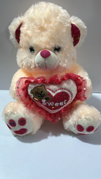 Urso de Pelúcia Bege Sentado com Detalhes Vermelhos nas Orelhas e Patas, Segurando Coração com Detalhes em Renda e Lantejoulas com a Inscrição Sweet. Aproximadamente 30cm.