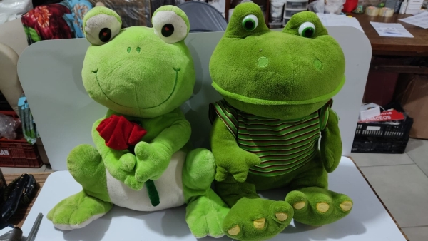 Par de Sapos de Pelúcia em Tons de Verde Sendo um com Flor Vermelha e Outro de Camiseta Listrada, Ideal para Decoração de Quarto Infantil ou Coleção. Aproximadamente 45cm de Altura.
