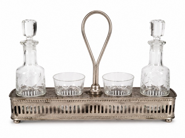 GALHETEIRO / CONJUNTO DE MESA EM ESTILO ART DÉCO – Conjunto em metal prateado, de desenho geométrico e linhas retas, composto por suporte retangular com alça central, dois frascos em vidro com tampas e dois recipientes em vidro para condimentos. Peça de gosto Art Déco, de apresentação elegante e funcional para o serviço de mesa. Medidas (base): 26 x 5,5 x 5,5 cm. Medida (azeiteiro): 15 cm alt. Medida (calice): 5 cm alt.