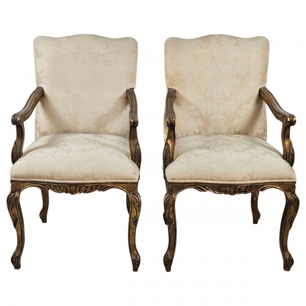 Elegante par de poltronas, de madeira entalhada e patinada a fino ouro. Apresenta assento e encosto estofados, braços que concluem em volutas, barra recortada, pernas sinuosas de joelheiras pronunciad