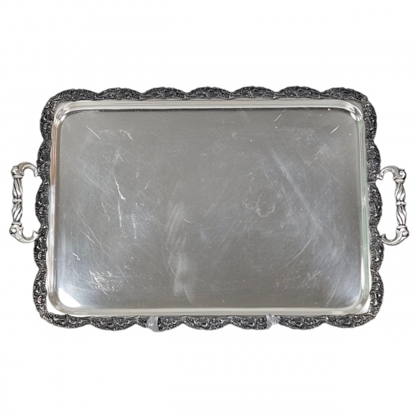 Bandeja de metal branco com banho de prata, formato retangular arredondada as quinas, alças vis a vis, borda recortada e ornamentada por flores, frutos e outros motivos fitomorfos. 63 x 40 cm. (Sinais