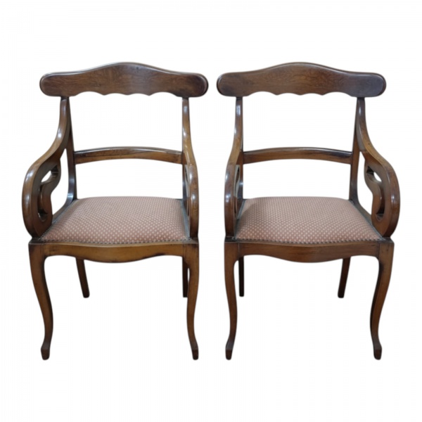 Par de cadeiras clássicas em madeira maciça, apresentando design refinado com estrutura em madeira trabalhada de alta qualidade e acabamento em tom natural. Os assentos estofados com Nailhead Trim. 52
