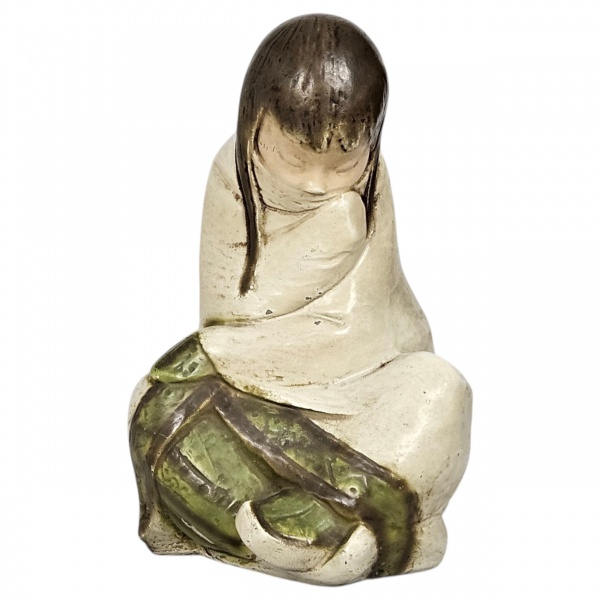 Estatueta representando uma menina esquimó sentada, confeccionada em cerâmica esmaltada, acabamento em tons terrosos, cabelos pretos simplificados e detalhes em esmalte verde oliva na base da vestimen