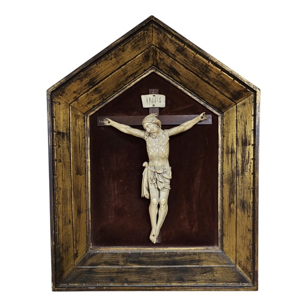 Magnífico crucifixo de madeira com Cristo esculpido em marfim, séc. XVII, moldura de madeira patinada e dourada no formato de nicho com bordas douradas e fundo vinho. Acima da cabeça de Cristo, uma pl